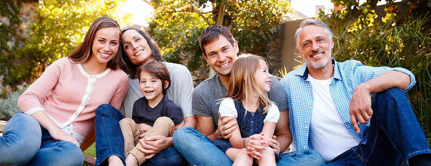 Pflege und Gesundheit: Familie über drei Generationen sitzt fröhlich im Garten unter Bäumen