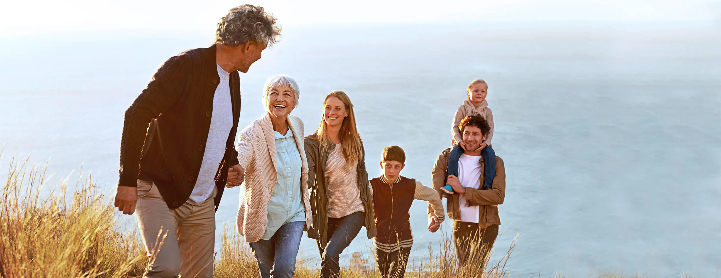 IDEAL Bestattungsvorsorge: Familie über drei Generationen geht Hand in Hand einen Hang vom Meer hinauf