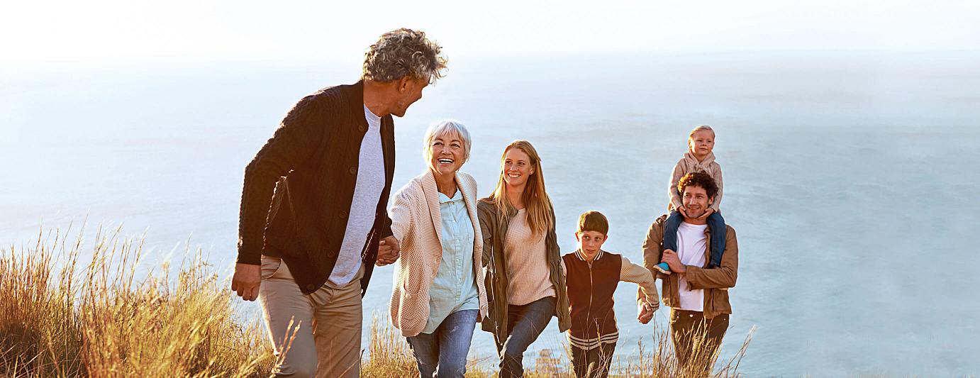 Bestattungsvorsorge: Familie über drei Generationen geht Hand in Hand einen Hang vom Meer hinauf